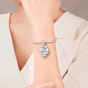 Macro detail of silver heart charm bracelet with engraved quote and pink gemstone