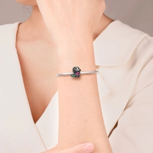 Detailansicht eines silbernen Schlangenarmbands mit schwarzem Dino-Anhänger und rosa Herzstein