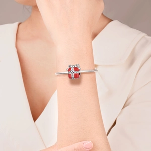 Close-up of silver snake chain bracelet with red enamel gift box charm and pink heart zircon