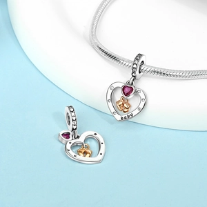 Detailed view of a silver heart charm with baby footprint and rose red crystal on a chain