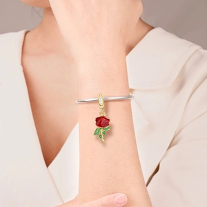 Detail of red enamel rose pendant with green crystal leaf on silver snake chain bracelet