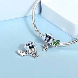 Detail of silver dragonfly and flower charm with blue enamel on snake chain bracelet