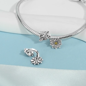 Close-up of silver snake chain bracelet featuring leaf charm and daisy pendant with yellow zircon