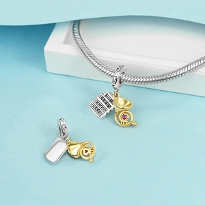 Detalle de amuleto musical de plata S925 con trompeta dorada y piedra de corazón rosa