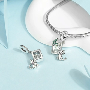 Macro detail of silver cat and green butterfly charms on a classic snake chain bracelet