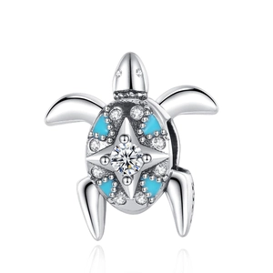Macro detail of a silver sea turtle charm with blue enamel shell and inlaid white zircon