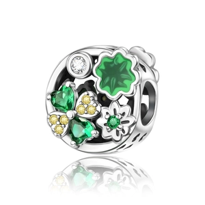 Macro detail of silver charm with green heart gems and enamel floral tree pattern