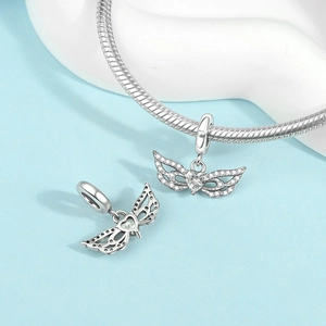 Detailed close-up of silver-plated angel wing charm with heart-shaped crystal stone