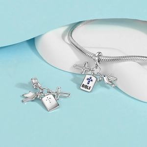 Detail of silver religious charms with bible, dove, and cross on a snake chain bracelet
