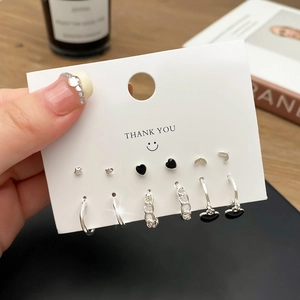 Detail eines silbernen Ohrring-Sets mit schwarzen Herzen und Perlen auf einer weißen Karte