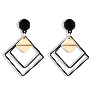 Detailed view of geometric drop earrings with black studs and gold squares on white background