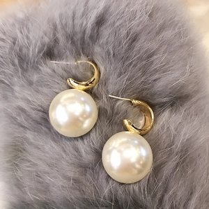 Elegante goldene gebogene Metall-Ohrhänger mit großen weißen Perlen auf grauem Samt