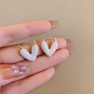 Elegant white enamel heart earrings in gold finish held between fingers for scale