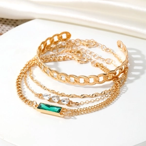 Dettaglio del set di quattro bracciali dorati con pietre verde smeraldo e cristalli chiari