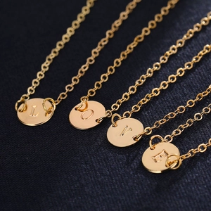 Set of four gold-toned necklaces with LOVE initial round pendants on a black textured background