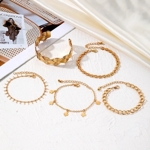 Five-piece gold metal cuff and clover charm bracelet set on minimalist white backdrop