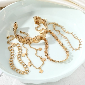 Five-piece gold jewelry set including woven bangle and heart pendant charms on white silk
