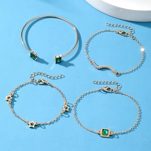 4-piece gold-tone bracelet set with emerald green crystals and star charms on blue background