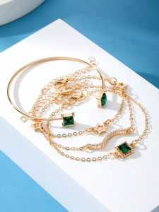 Close-up of gold bracelet set featuring emerald square stones and star charms