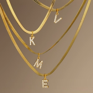 Close-up of gold herringbone chain necklaces with zircon-studded initial pendants