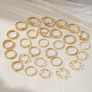 Golden 25-piece geometric ring set with heart and pearl accents on white marble surface