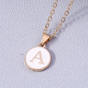 Macro de un collar dorado con colgante redondo de esmalte blanco y la letra inicial A