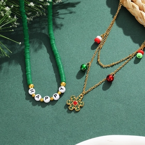 Detail von zwei Weihnachtshalsketten mit grünen Perlen und Goldglöckchen auf grünem Grund