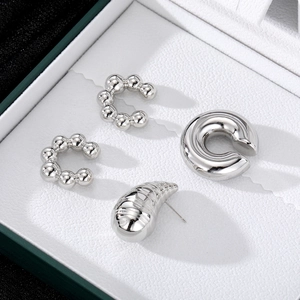 Polierte silberne Tropfenohrringe und kugelförmige Earcuffs auf weißer Geschenkbox