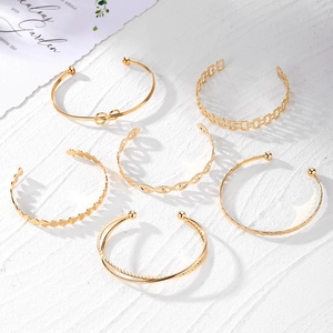 6er-Set goldene Armreifen mit Herz- und Knoten-Design auf weißem Marmorhintergrund