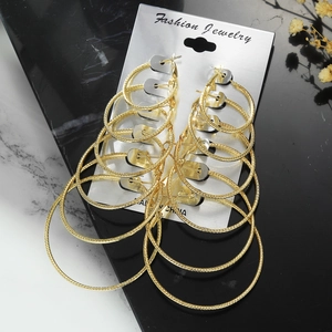 Detail of 6 pairs golden hoop earrings set with diamond pattern texture on marble background