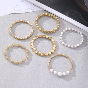 Set aus sechs goldenen Perlenarmbändern im Boho-Stil auf grauem Hintergrund
