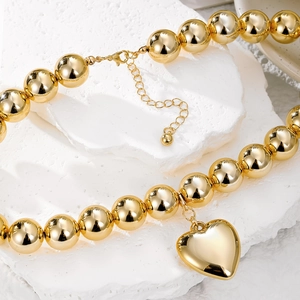 Punk style golden bead necklace with smooth heart pendant on white marble stone