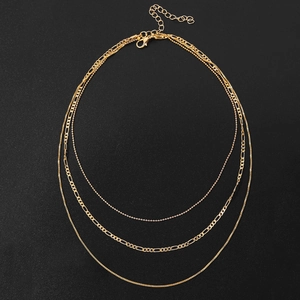 Gros plan sur collier doré multi-rangs avec mailles Figaro et boules sur fond noir