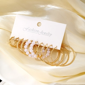 Set de 6 pares de pendientes dorados de aro con perlas sobre fondo de seda crema