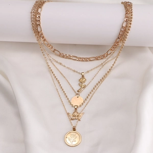 Layered gold necklace set with angel, rose, and coin pendants on elegant silk fabric