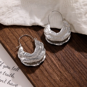 Macro detail of textured silver metal earrings with artistic molten lava surface design
