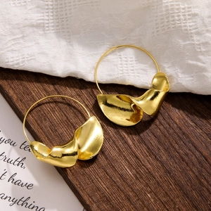Detail of matte gold hoop earrings with twisted metal leaves on dark wood background