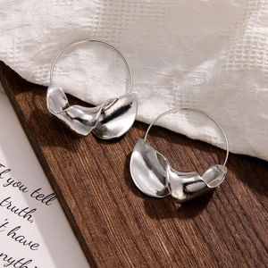 Detail view of silver metal leaf earrings with twisted texture on wood and fabric