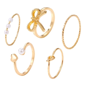 Parure de 5 bagues dorées avec perles, nœuds et motifs en cœur sur un fond blanc neutre