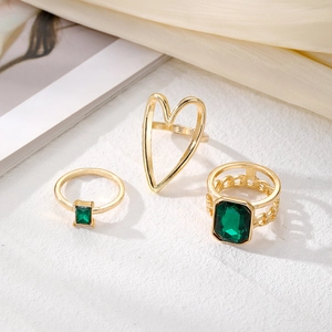 Golden ring set featuring emerald green gems and hollow heart design on silk background