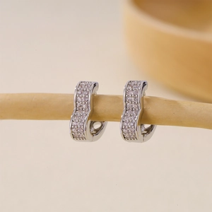 Elegantes pendientes de aro en plata con forma de onda y circonitas sobre rama madera