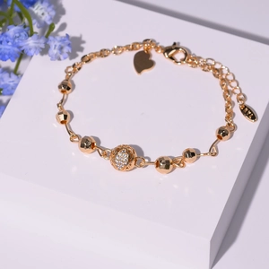 Détail du bracelet plaqué or avec une sphère creuse en zircon et un pendentif coeur