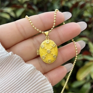 Détail d'un médaillon floral plaqué or 18K avec émail jaune sur une chaîne à billes