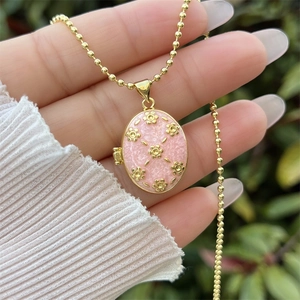 Collier médaillon ovale plaqué or 18K avec émail rose et motif floral tenu à la main