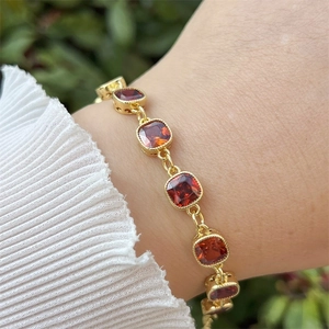Detail of red cushion-cut gemstones with bead-edge setting on gold-plated bracelet