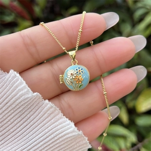 Primer plano de cadena dorada con un relicario de esmalte azul y motivos florales