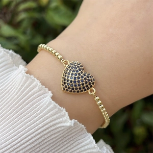 Primer plano de pulsera bañada en oro de 18k con dije de corazón de circón azul en muñeca