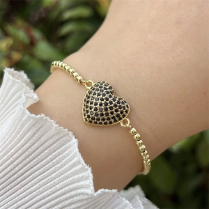 Detalle de pulsera de cuentas de oro 18k con colgante de corazón negro en la muñeca