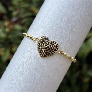 Macro de una pulsera bañada en oro de 18k con un colgante de corazón negro y circonitas