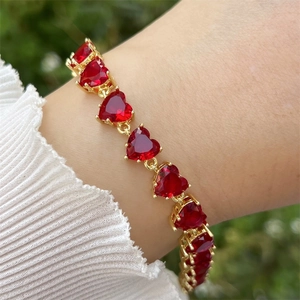 Nahaufnahme des vergoldeten Armbands mit herzförmigen roten Zirkonsteinen im eleganten Stil